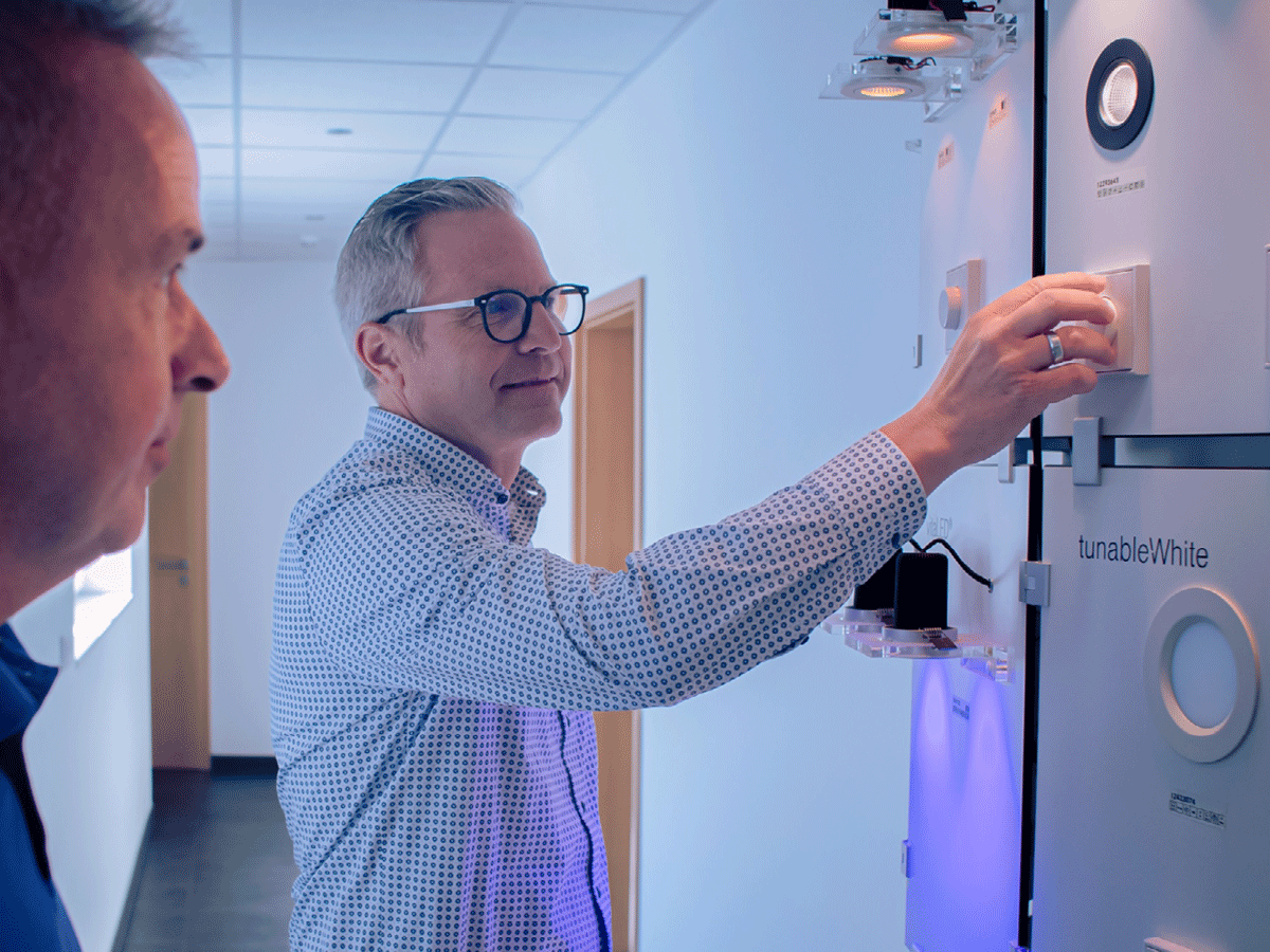 EGU-Niederlassungsleiter zeigt einem Kunden einen Dimmer und Deckenleuchtenm, die an einer Wand montiert sind.